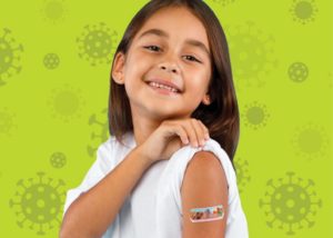 Une petite fille souriante relève la manche de son t-shirt et montre fièrement le pansement sur son bras après avoir reçu un vaccin. Arrière-plan vert pâle avec motifs de coronavirus.