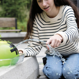 Fille qui fait l'expérience du jet d'eau continu avec un ballon rempli et percé.