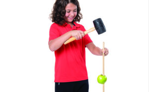 Un jeune qui cogne avec un marteau sur une tige de bois pour faire descendre une pomme sur laquelle elle est insérée